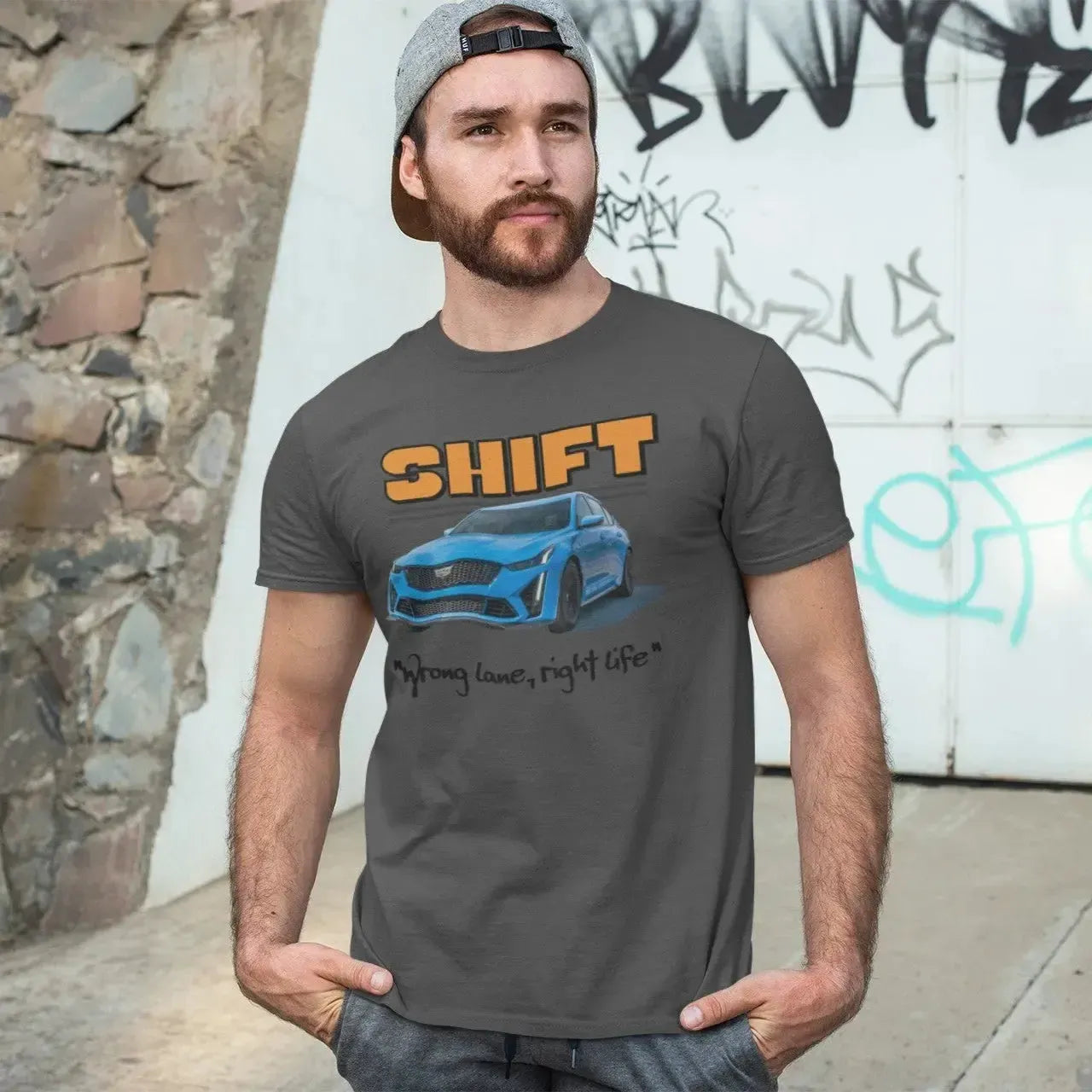 Man wearing a t-shirt with 'SHIFT' graphic design in front of a graffiti-covered wall.